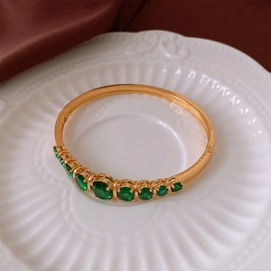 Vue détaillée d'un bracelet doré orné de gemmes vertes sur un plat en céramique blanc