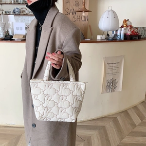 Close-up of quilted cream tote bag with rabbit ear pattern held by a model in a cafe