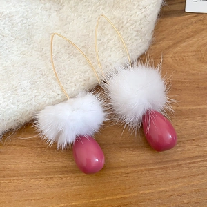Dettaglio di orecchini eleganti con pompon bianco e ciondolo a goccia rosa scuro in primo piano