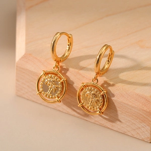 Detail of gold coin earrings featuring a palm tree motif on a wooden pedestal