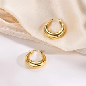 Detail of polished gold crescent hoop earrings on beige silk and stone background