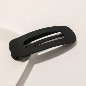 Macro shot of minimalist matte black hair clip with geometric cutout on white surface