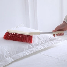 Detail of red bristle long-handle cleaning brush sweeping on white pillow surface