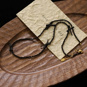 Detail of black beaded necklace with bows and gold stainless steel clasp on wood