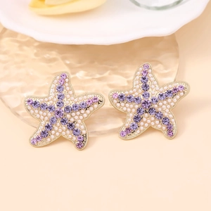 Détail de boucles d'oreilles étoile de mer avec strass violets et perles blanches