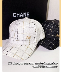 Detail of tweed baseball caps in black and white with gold metallic M logo letters