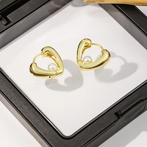 Détail macro de boucles d'oreilles cœur dorées avec perles blanches en écrin