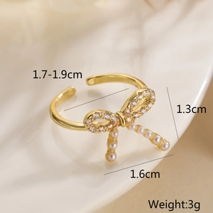 Detailed view of gold bow ring with cubic zirconia and pearl on a beige surface