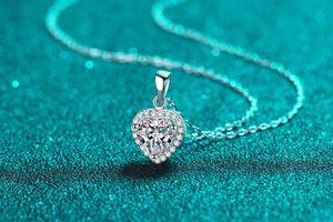 Vue macro d'un collier pendentif cœur en moissanite avec sertissage halo sur fond bleu sarcelle