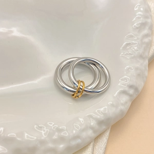 Close-up of interlocking silver bands with gold ring accents on white ceramic tray