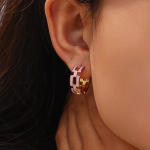 Close-up of gold geometric chain earrings with purple enamel inlay on a female model