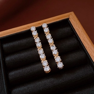 Macro detail of gold tassel earrings with round zircons and X-shaped metal links