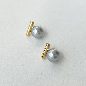 Nahaufnahme eleganter grauer Perlenohrringe mit polierten goldenen Metallstäben
