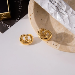 Detail of golden heart knot stud earrings on a stone tray with elegant props