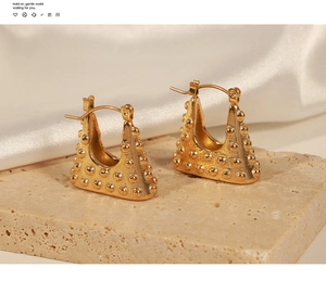 Close-up of golden geometric triangle earrings with polka dot texture on stone base
