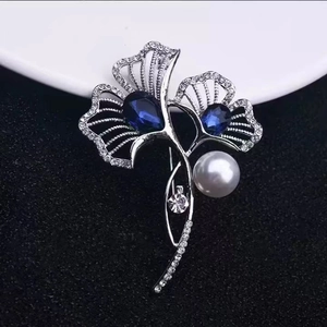 Detailed view of silver ginkgo leaf brooch with blue teardrop stones and pearls
