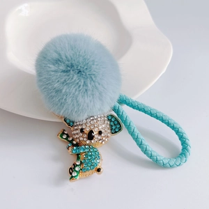 Detailed close-up of a blue fluffy koala keychain with rhinestones and woven leather strap