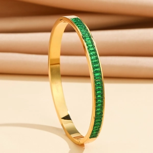 Macro shot of gold stainless steel bangle featuring emerald-cut green cubic zirconia stones