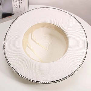 Detail of white straw hat with black trim and pearl accents, featuring internal sweatband