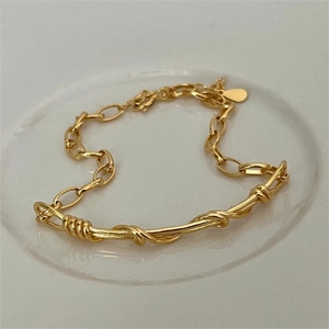Detail of a minimalist gold handmade braided twist bar bracelet with delicate metal chain