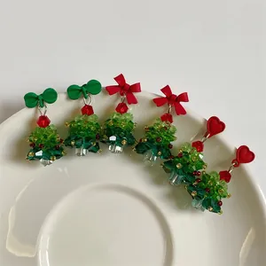 Macro detail of handmade beaded Christmas tree earrings with red bows on white plate