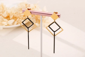 Detail of geometric drop earrings with gold and black square nested frames on a stand