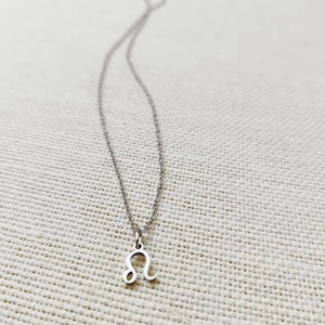 Detail of silver Leo zodiac symbol pendant on stainless steel chain over linen fabric