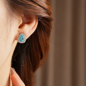 Close-up of elegant teardrop blue zircon earring with white stone halo on female model