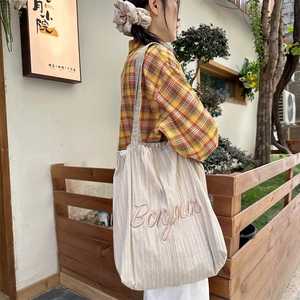Detail of striped canvas tote with Bonjour embroidery and wide strap in outdoor setting