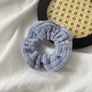 Close-up of a grey knitted velvet scrunchie on white textured fabric for hair styling