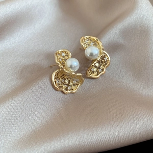 Detail of twisted hollow butterfly earrings with white pearls and zircons on champagne satin