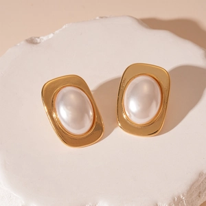 Detailed close-up of vintage gold metal earrings with large pearls on a white stone pedestal