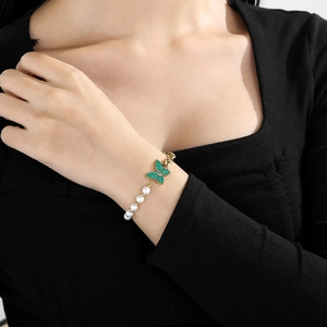 Detail of vintage gold chain bracelet with green enamel butterfly and pearls on wrist
