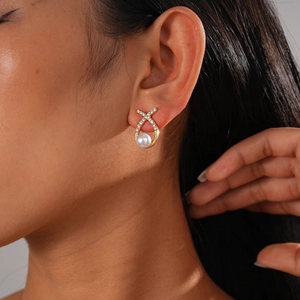 Close-up of golden X-shaped stud earring with pavé crystals and round pearl detail