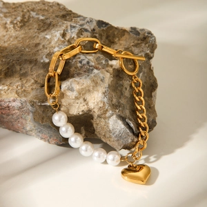 Detail of gold chain bracelet with white pearls and heart pendant on stone