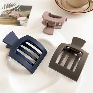 Three matte rectangular hair claws in navy, brown, and pink on a white porcelain plate