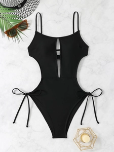 Flat lay of black cutout one-piece swimsuit with lace-up details on marble background