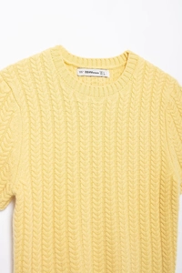 Dettaglio dello scollo rotondo e della trama a trecce di questo maglione giallo alla moda
