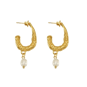 Macro detail of U-shaped gold earrings with irregular texture and white baroque pearls