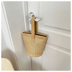 Detail of hand-woven straw bucket bag featuring a brown leather handle on a white door