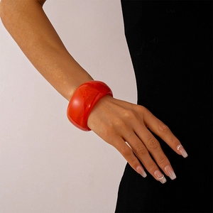 Detail of wide orange-red acrylic bangle with marble pattern worn on a model wrist