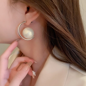 Close-up of stylish C-shaped silver earrings with a large white pearl on a female model