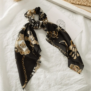 Detail of a black satin scrunchie with a gold chain pattern and long streamers