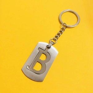Top view of hollow letter B stainless steel keychain with ring on yellow background