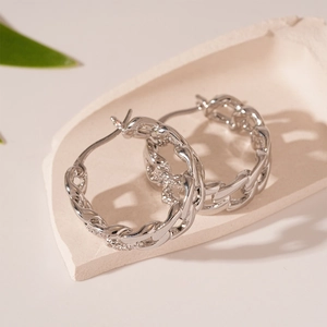 Detailed view of silver braided chain link hoop earrings on a decorative stone base
