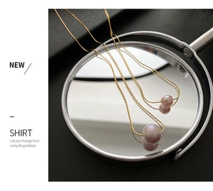 Close-up of pinkish freshwater pearl on a fine gold chain reflected on a mirror surface