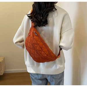 Rear view of an orange quilted crossbody bag worn over a white hoodie in a stylish setting