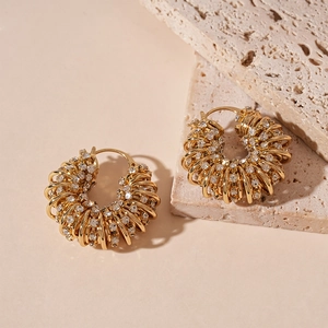 Détail macro des boucles d'oreilles créoles dorées en U avec strass brillants sur travertin
