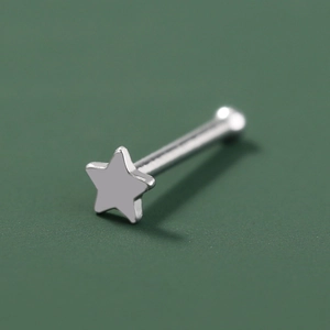 Macro shot of silver stainless steel star-shaped nose stud on a textured green background