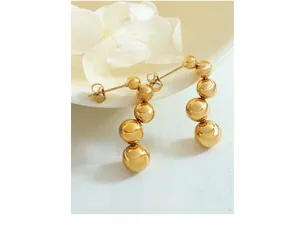 Detail shot of elegant polished gold ball drop earrings on white ceramic tray decor